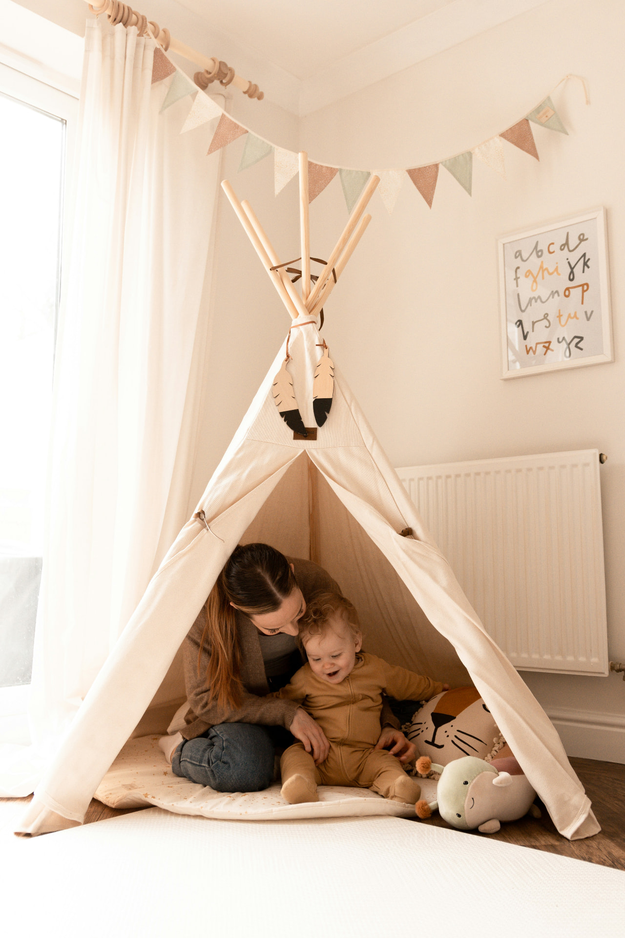 A mother and her baby playing together inside a soft blue and cream play teepee