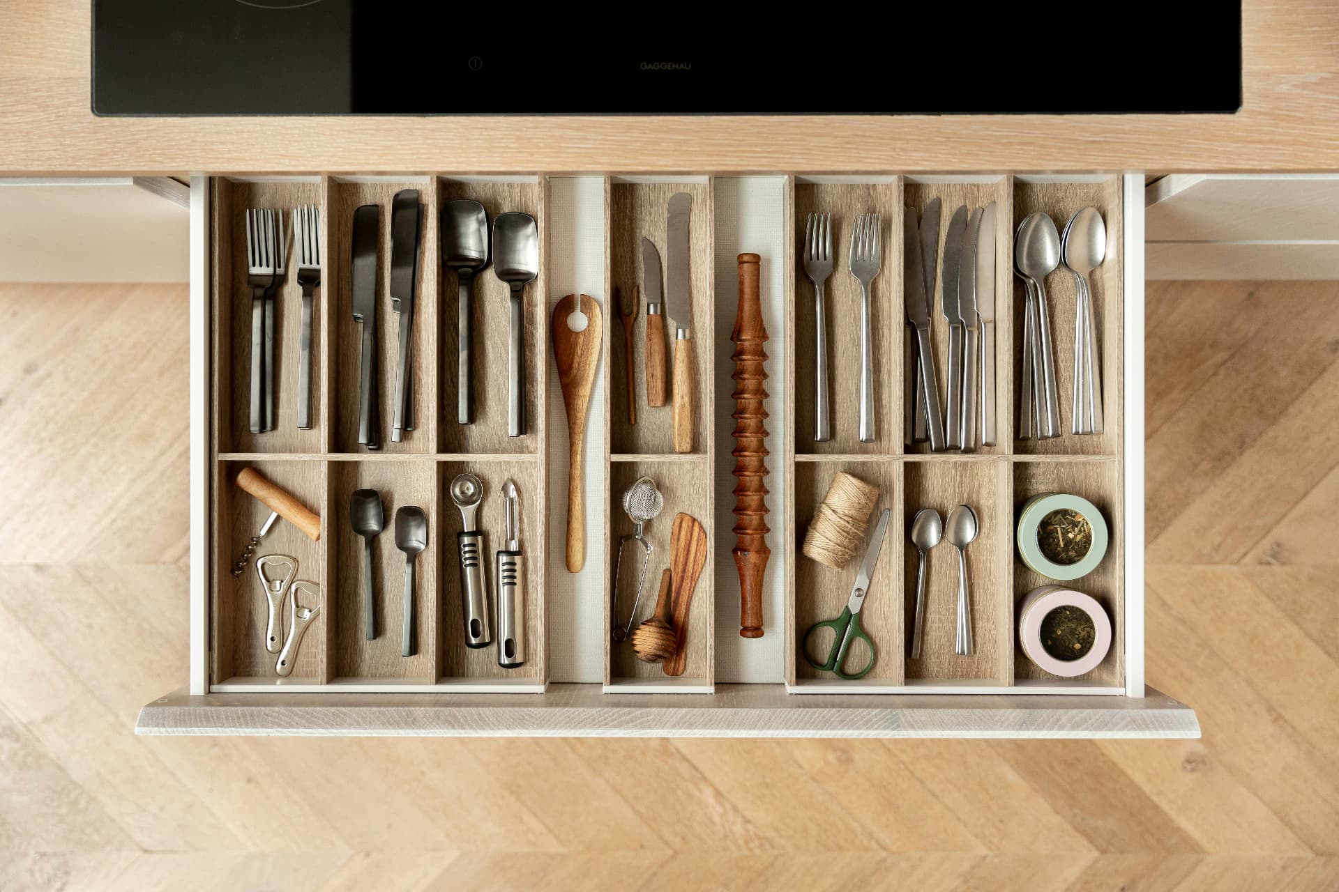 A kitchen drawer with cutlery and utensils arranged in oak dividers