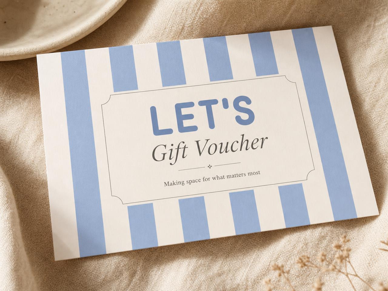 A LET'S Organise gift voucher with soft cornflower blue and cream stripes, held over a warm linen surface